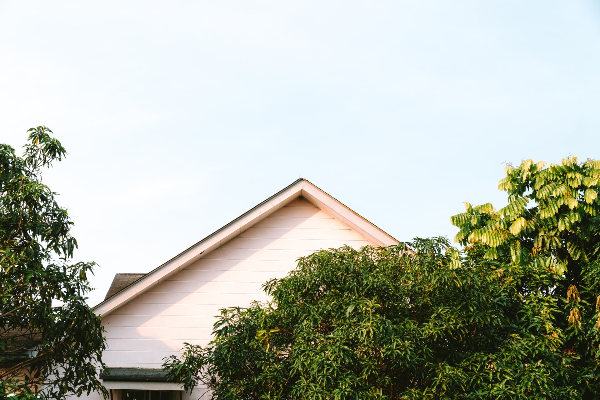 A serene view of a house framed by lush trees against a clear sky, evokes a sense of suburban tranquility.