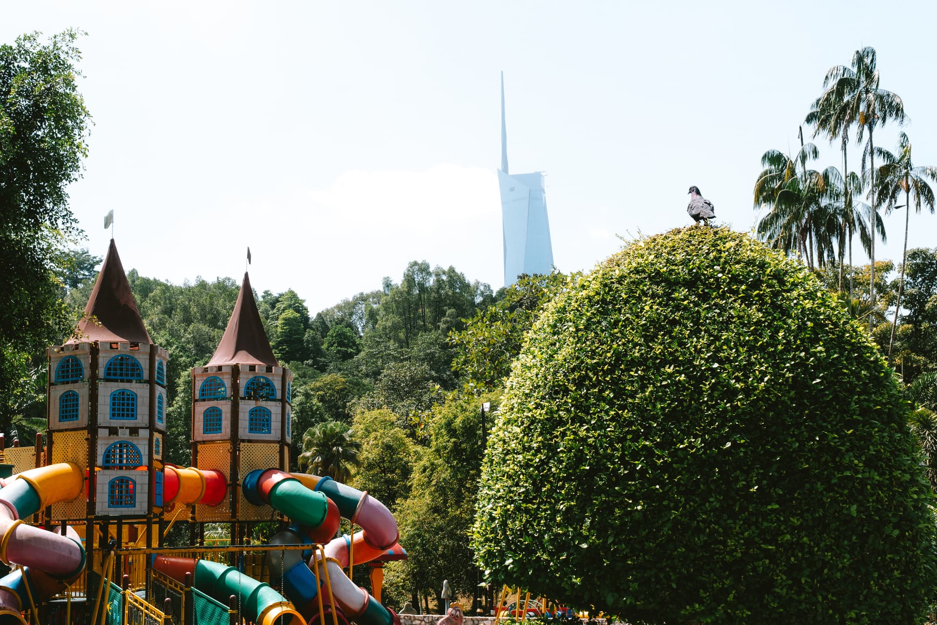A playful scene with a castle playground and a pigeon perched atop a green bush.