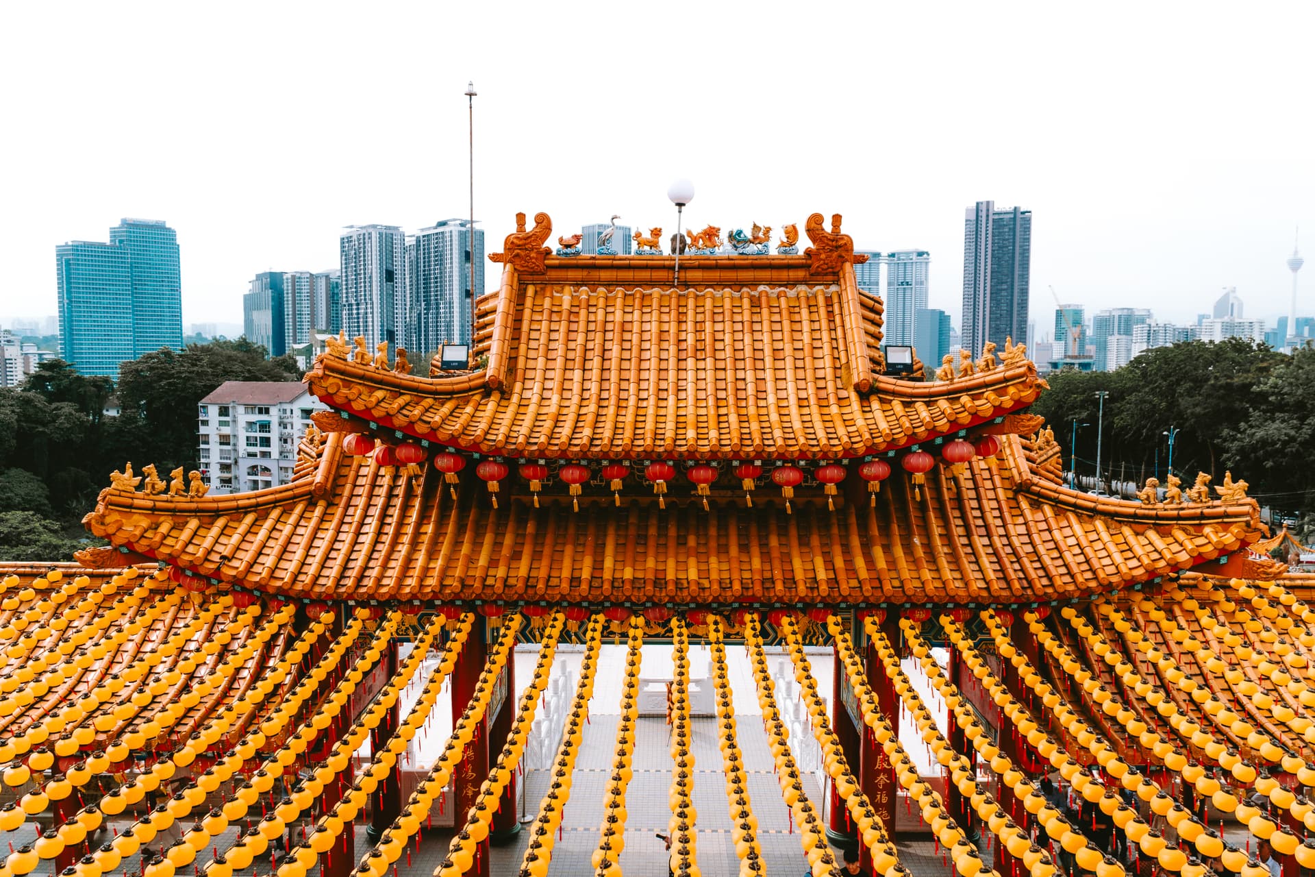 A stunning architectural shot of a temple roof, adorned with lanterns, against the backdrop of a modern city.