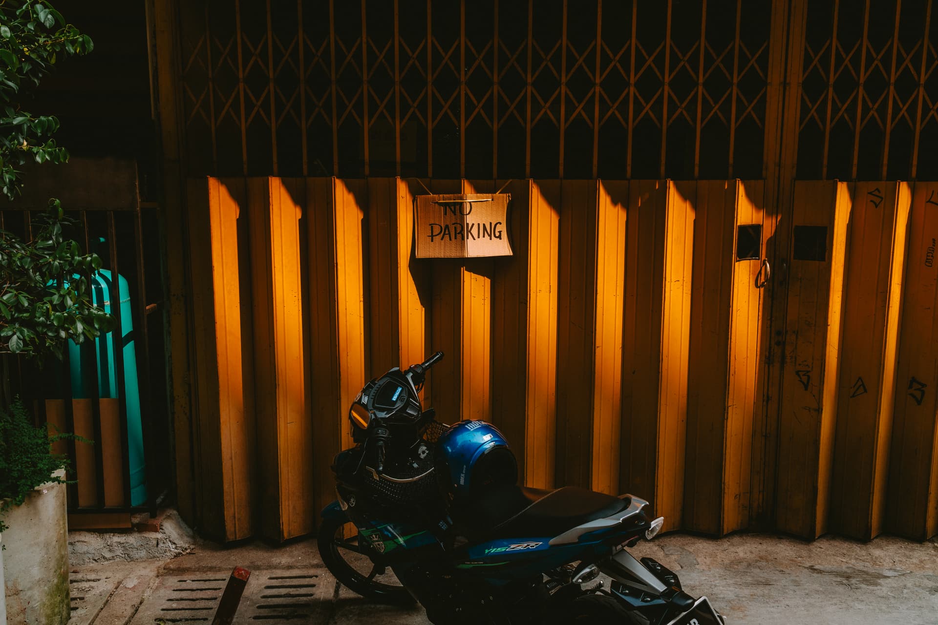 A motorcycle parked in front of a gate with a no parking sign.